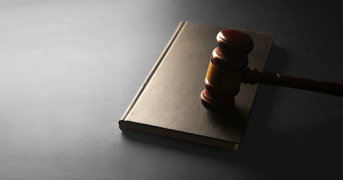 Wooden judge's gavel resting on a closed dark hardback book on a grey surface with soft side lighting